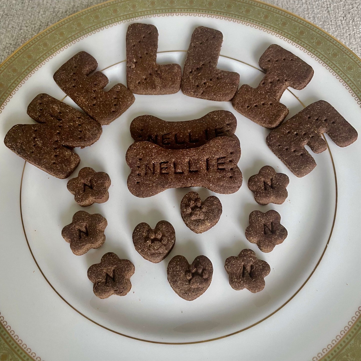 A white plate with dog cookies in the shape of the dog's name, dog bones, mini flowers, and mini hearts.