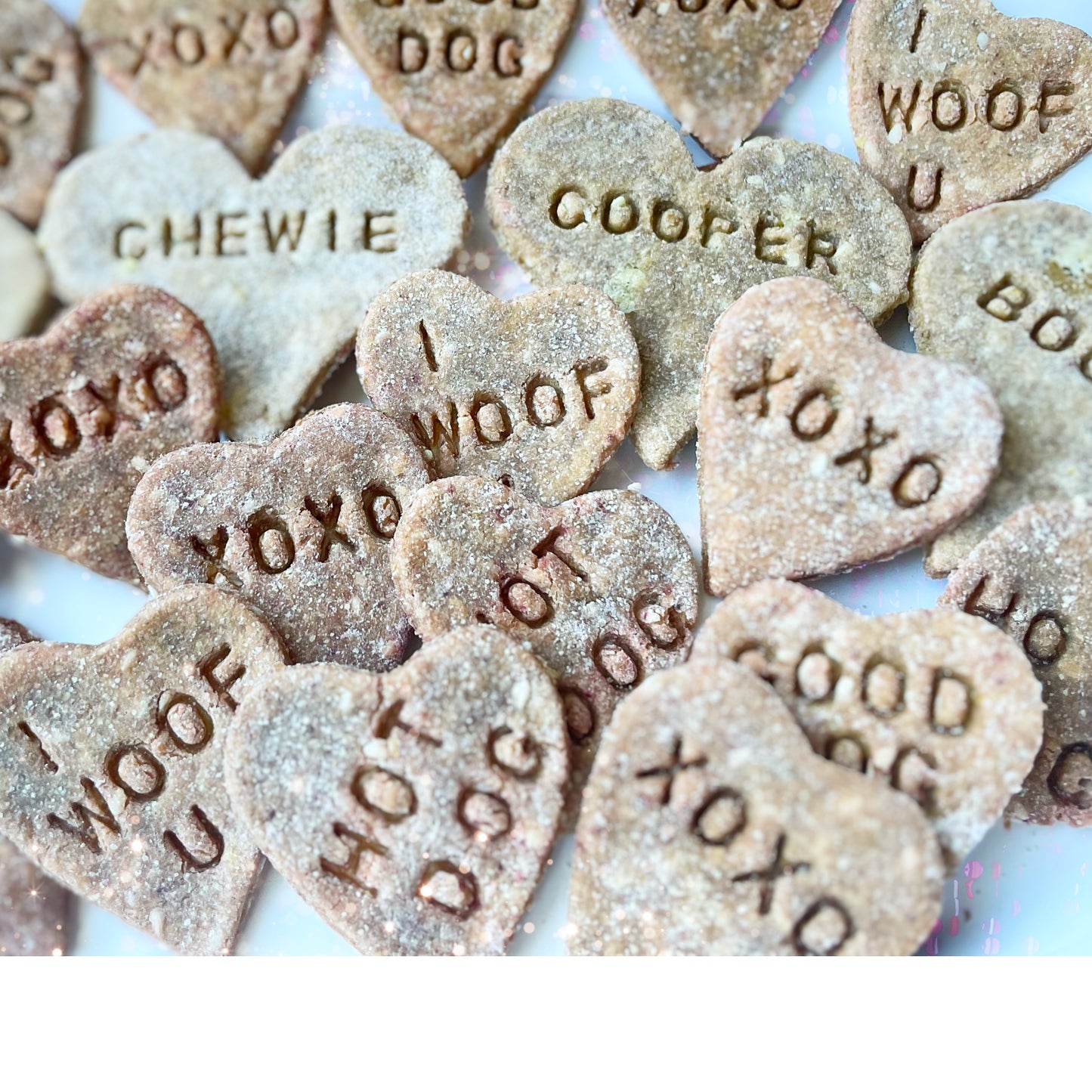 Valentine's Day heart-shaped dog cookies personalized with dogs' names as well as "XOXO," "HOT DOG," and "I WOOF YOU."
