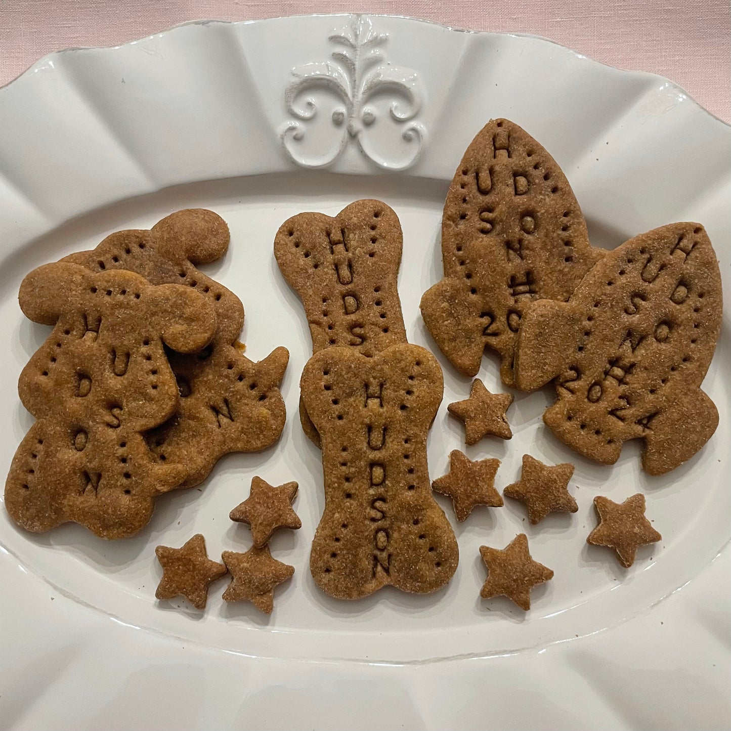 Large peanut butter dog cookies in the shapes of two dogs, two dog bones, and two rocket ships. All cookies are personalized with the name, "HUDSON."