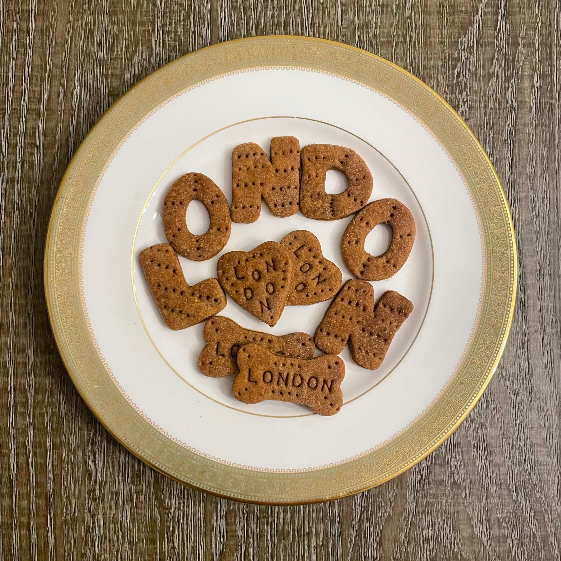 Medium peanut butter dog cookies in the shapes of two hearts and two dog bones, all personalized with the name, "LONDON." Additionally, each letter of the name, London, has been cut into a cookie to further enhance the unique quality of this product.