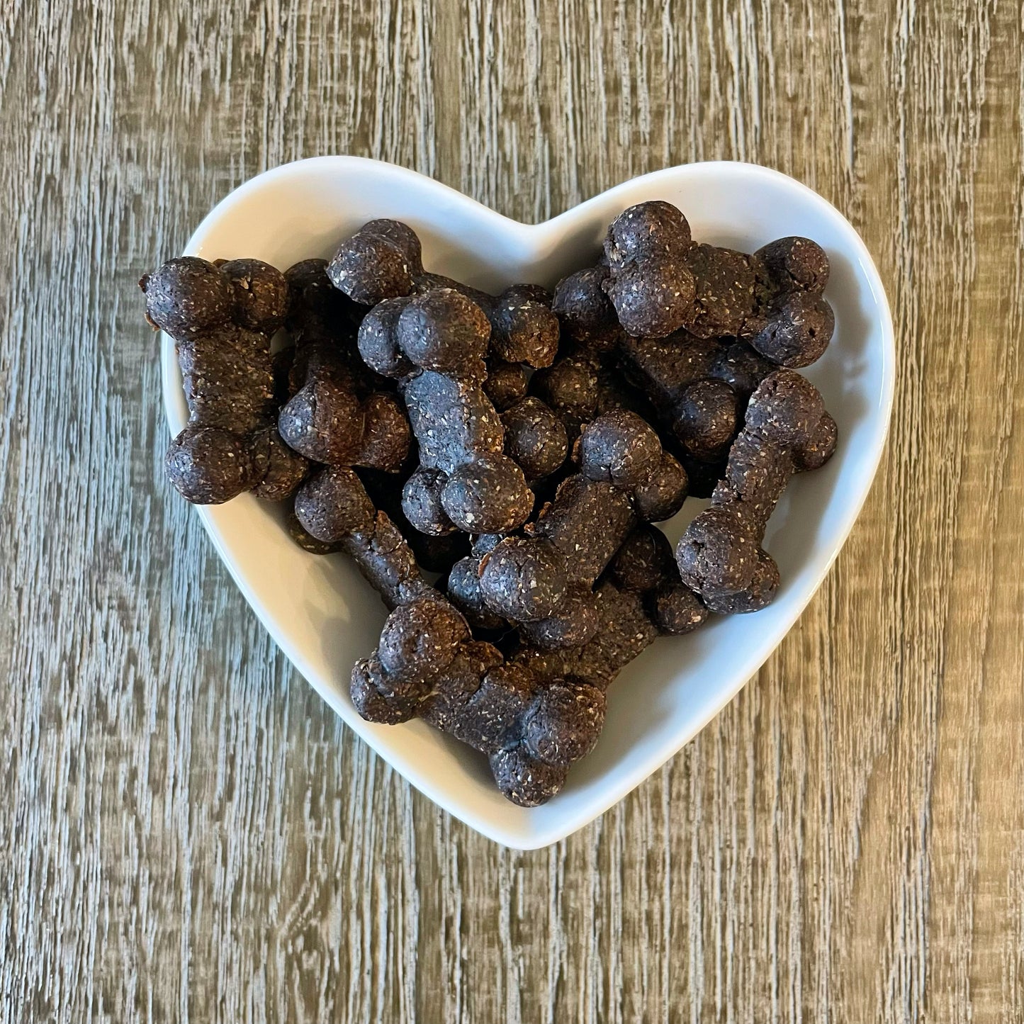 A heart-shaped white bowl filled with dark brown dog bone-shaped cookies.