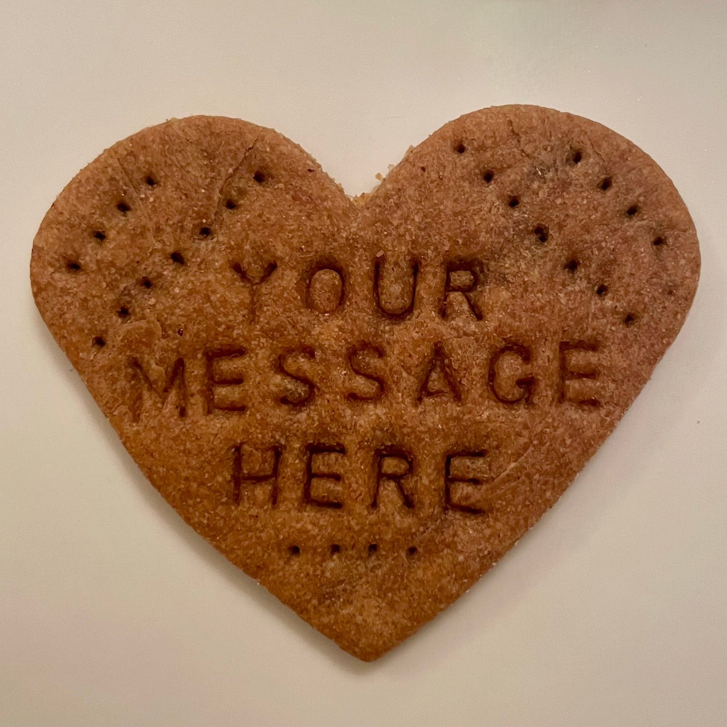 A dog cookie in the shape of a heart with "Your Message Here" personalized on it.